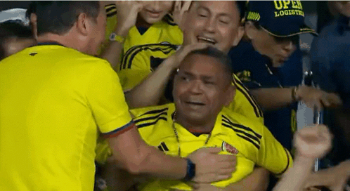 A Man In A Yellow Adidas Shirt Is Being Hugged By A Crowd GIF