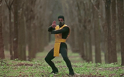 A Man In A Yellow And Black Costume Is Standing In The Woods Holding A Long Sword . GIF