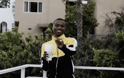 A Man In A Yellow And Black Jacket Is Holding A Cup That Says ' Almost Naked ' On It GIF