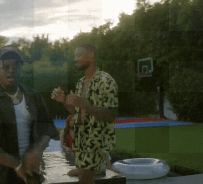 A Man In A Yellow And Black Shirt Stands Next To Another Man In A Black Shirt GIF