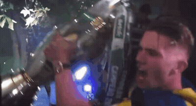 A Man In A Yellow And Blue Shirt Is Holding A Large Trophy In His Mouth GIF