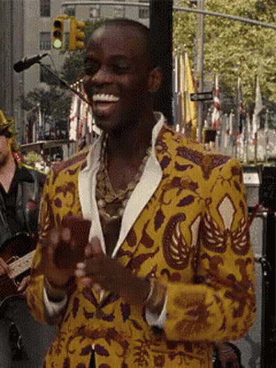 A Man In A Yellow And Purple Jacket Is Smiling And Holding A Cell Phone GIF