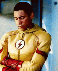 A Man In A Yellow And Red Flash Suit Is Standing With His Arms Crossed . GIF