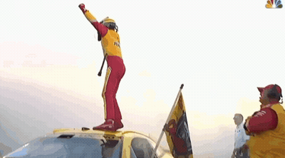 A Man In A Yellow And Red Racing Suit Is Dancing In Front Of A Crowd . GIF