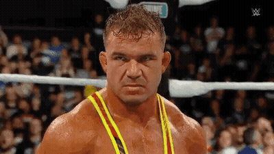 A Man In A Yellow And Red Tank Top Is Standing In A Wrestling Ring Looking At The Camera . GIF