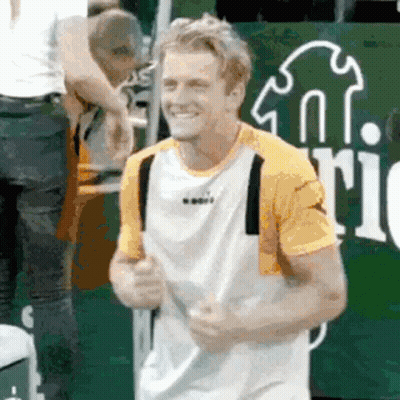 A Man In A Yellow And White Shirt Is Smiling While Holding A Tennis Racket . GIF