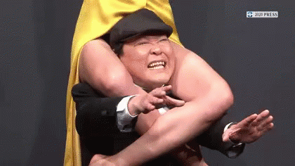 A Man In A Yellow Cape Is Being Held By Another Man In A Black Suit . GIF