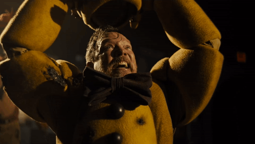 A Man In A Yellow Costume With A Bow Tie Is Screaming In The Dark GIF