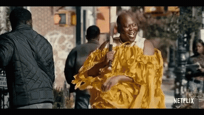 A Man In A Yellow Dress Is Holding A Microphone And Smiling . GIF