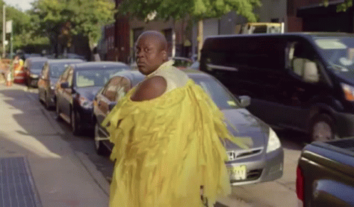 A Man In A Yellow Dress Is Walking Down A Busy Street GIF