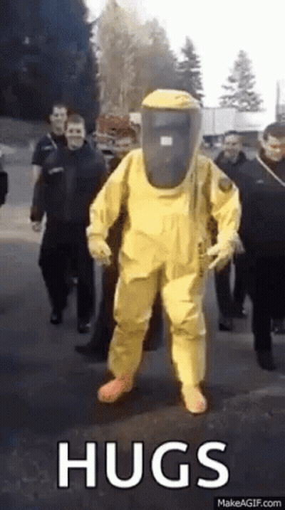 A Man In A Yellow Hazmat Suit Is Walking Down A Street . GIF