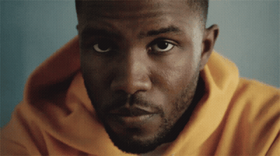 A Man In A Yellow Hoodie Looks At The Camera GIF