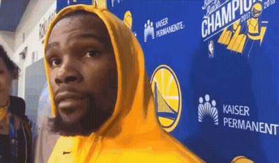 A Man In A Yellow Hoodie Stands In Front Of A Kaiser Permanente Sign GIF