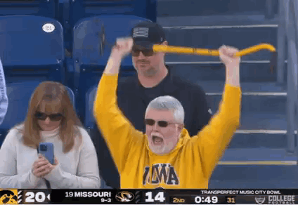 A Man In A Yellow Iowa Shirt Holds A Yellow Stick In The Air GIF