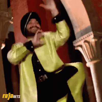 A Man In A Yellow Jacket And Black Hat Is Dancing In Front Of A Sign That Says Rajabets On It GIF