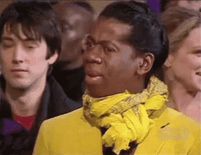 A Man In A Yellow Jacket And Scarf Is Making A Funny Face . GIF