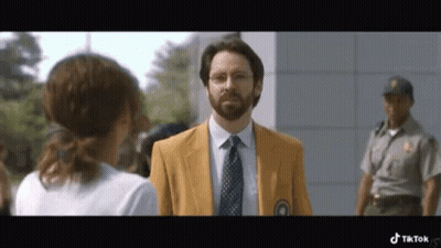 A Man In A Yellow Jacket And Tie Is Talking To A Woman While A Police Officer Stands Behind Him . GIF