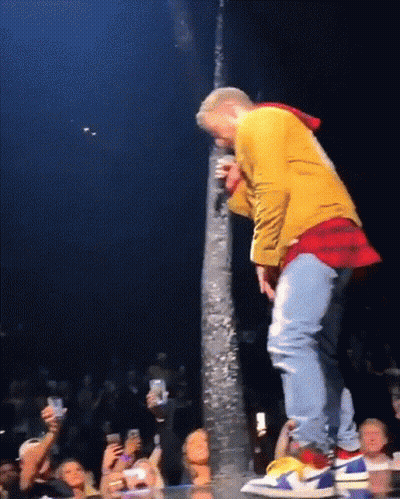 A Man In A Yellow Jacket Is Singing Into A Microphone While Standing On A Stage GIF