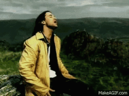 A Man In A Yellow Jacket Is Sitting On Top Of A Hill . GIF