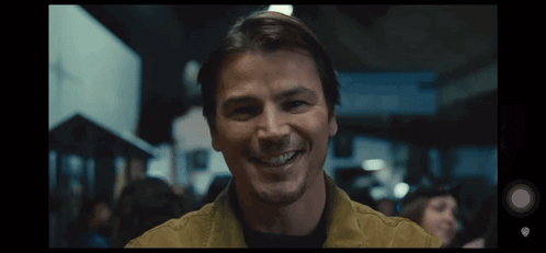 A Man In A Yellow Jacket Is Smiling In A Crowd GIF