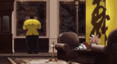 A Man In A Yellow Jacket Is Standing In A Living Room Looking Out A Window . GIF