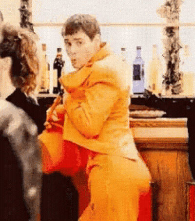 A Man In A Yellow Jacket Is Standing In Front Of A Bar GIF
