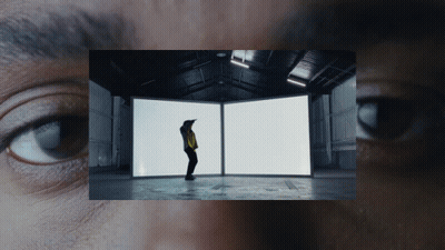 A Man In A Yellow Jacket Is Standing In Front Of Two White Boxes GIF