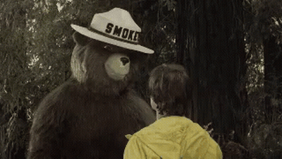 A Man In A Yellow Jacket Is Standing Next To A Bear In The Woods GIF
