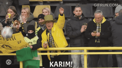 A Man In A Yellow Jacket Says Karim In Front Of A Group Of People GIF