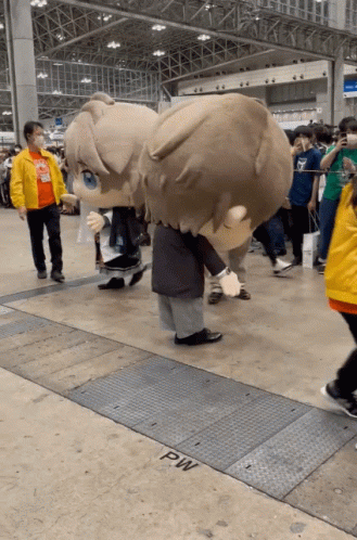 A Man In A Yellow Jacket Stands Next To A Giant Stuffed Animal That Says Pw GIF