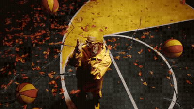 A Man In A Yellow Jacket Stands On A Basketball Court Surrounded By Basketballs And Leaves GIF