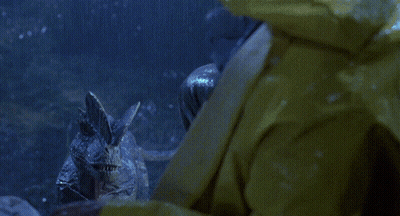 A Man In A Yellow Raincoat Is Being Attacked By A Dinosaur In Front Of A Jeep That Says Good Year GIF