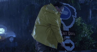 A Man In A Yellow Raincoat Is Standing Next To A Sign That Says East Dock GIF