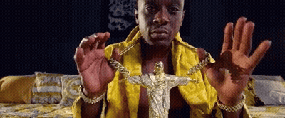 A Man In A Yellow Robe Is Holding A Gold Jesus Pendant GIF
