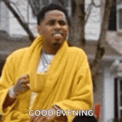 A Man In A Yellow Robe Is Saying `` Good Evening '' While Holding A Cup Of Coffee . GIF