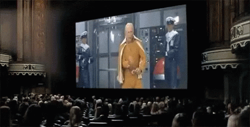 A Man In A Yellow Robe Is Standing In Front Of A Large Screen In An Auditorium .. GIF