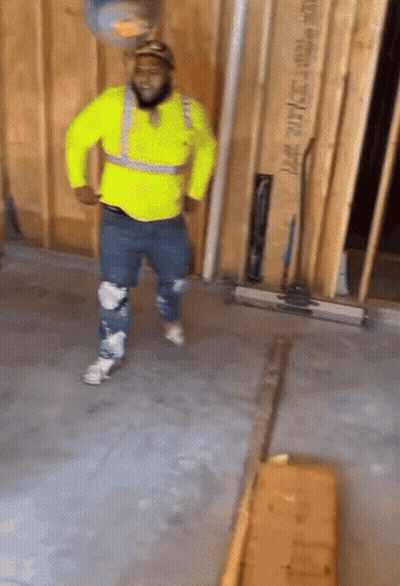 A Man In A Yellow Safety Vest Is Dancing In A Room With A Wall That Says Lmt 2014 On It GIF