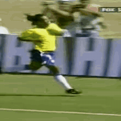A Man In A Yellow Shirt And Blue Shorts Is Running On A Soccer Field In Front Of A Sign That Says Fox GIF