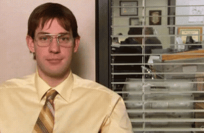 A Man In A Yellow Shirt And Tie Is Standing In Front Of A Window With Blinds . GIF