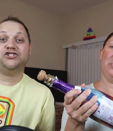 A Man In A Yellow Shirt Holds A Purple Bottle Of Wine GIF