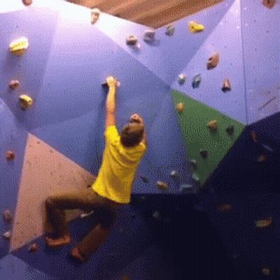 A Man In A Yellow Shirt Is Climbing Up A Climbing Wall GIF