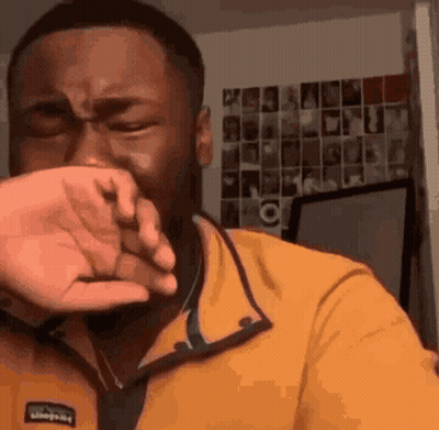 a man in a yellow shirt is covering his face with his hand .