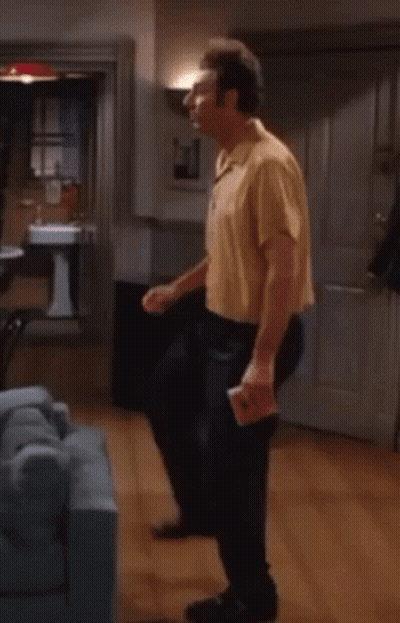 A Man In A Yellow Shirt Is Dancing In A Living Room With A Blue Couch . GIF