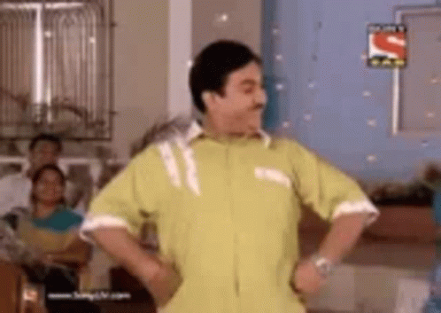 A Man In A Yellow Shirt Is Dancing In A Room . GIF