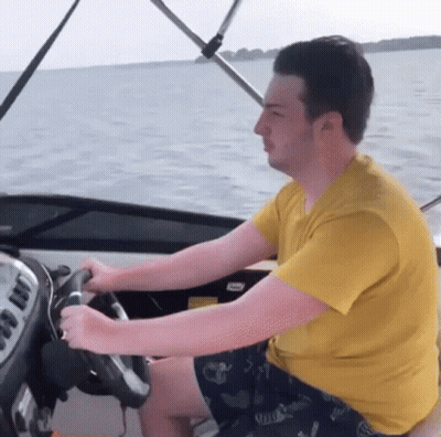 A Man In A Yellow Shirt Is Driving A Boat In The Ocean GIF