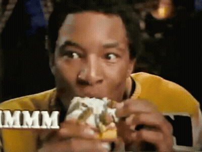 A Man In A Yellow Shirt Is Eating A Hamburger With The Word Mmmm In The Background GIF