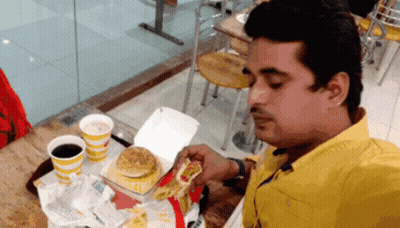 A Man In A Yellow Shirt Is Eating A Mcdonald 'S Burger GIF