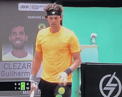 A Man In A Yellow Shirt Is Holding A Tennis Racquet In Front Of A Scoreboard That Says Clezar Guilherme GIF