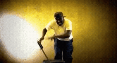 A Man In A Yellow Shirt Is Holding A Vacuum Cleaner While Dancing . GIF