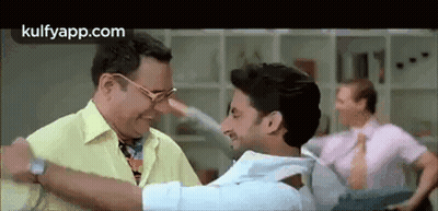 A Man In A Yellow Shirt Is Hugging Another Man In A Room . GIF